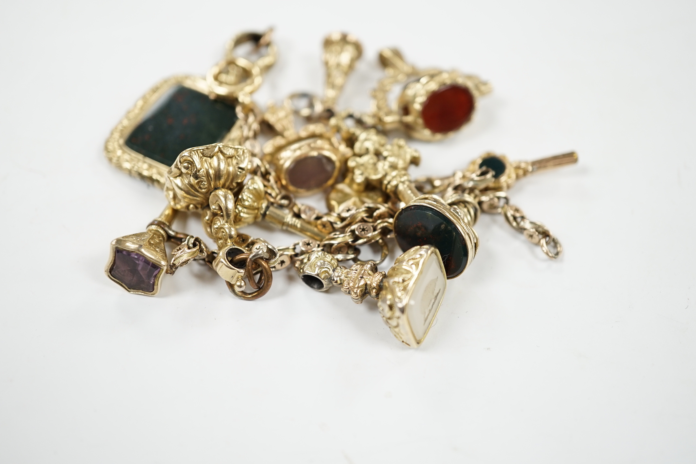 An early 20th century yellow metal charm bracelet (a.f.), hung with five assorted watch keys, together with seven assorted yellow metal overlaid and chalcedony set fobs.